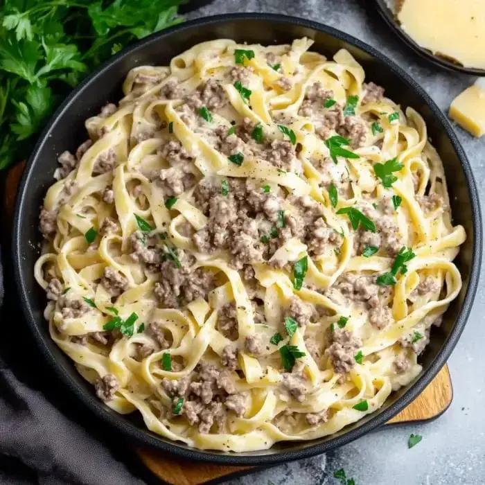 Beef Alfredo pasta with parsley in a black bowl